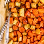 overhead view of a parchment lined baking sheet full of roasted root vegetables with a fork and spoon in the pan - 10