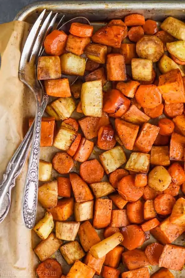 overhead view of a parchment lined baking sheet full of roasted root vegetables with a fork and spoon in the pan