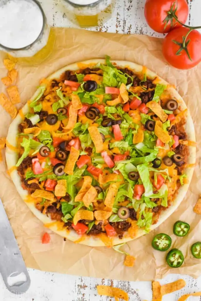 overhead view of a whole taco pizza with jalapeños and chips and beer around it