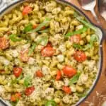 overhead photo of a skillet with a red handle holding an easy skillet chicken pesto pasta recipe, garnished with fresh Parmesan and fresh basil