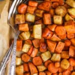 overhead view of a parchment lined baking sheet full of roasted root vegetables with a fork and spoon in the pan