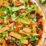 close up overhead view of a taco pizza that is topped with lettuce, chips, tomatoes, olives and green onions