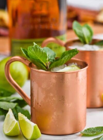 a copper mug filled with ice for a Kentucky mule, garnished with mint leaves, two lime wedges next to it