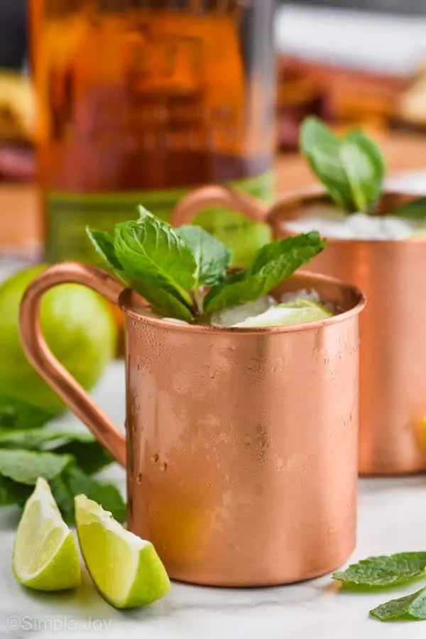 a copper mug filled with ice for a Kentucky mule, garnished with mint leaves, two lime wedges next to it