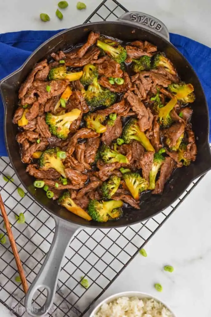 overhead photo of a gray skillet on a wire cool rack with a blue napkin holding beef and broccoli garnished with scallions