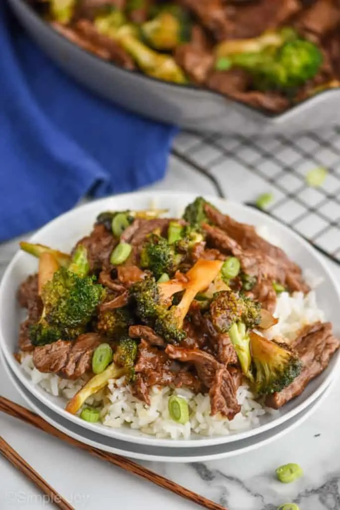 overhead photo of two white plates with white rice and beef and broccoli stir fry with a wire cooling rack in the background and a cloth blue napkin