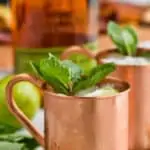 a copper mug filled with ice for a Kentucky mule, garnished with mint leaves, two lime wedges next to it