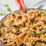 side view of a red skillet full of easy rice and beans recipe, garnished with cilantro