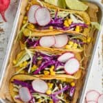 overhead of four vegan black bean tacos on a rimmed baking tray, garnished with sliced radishes, shredded cabbage, and corn - 6