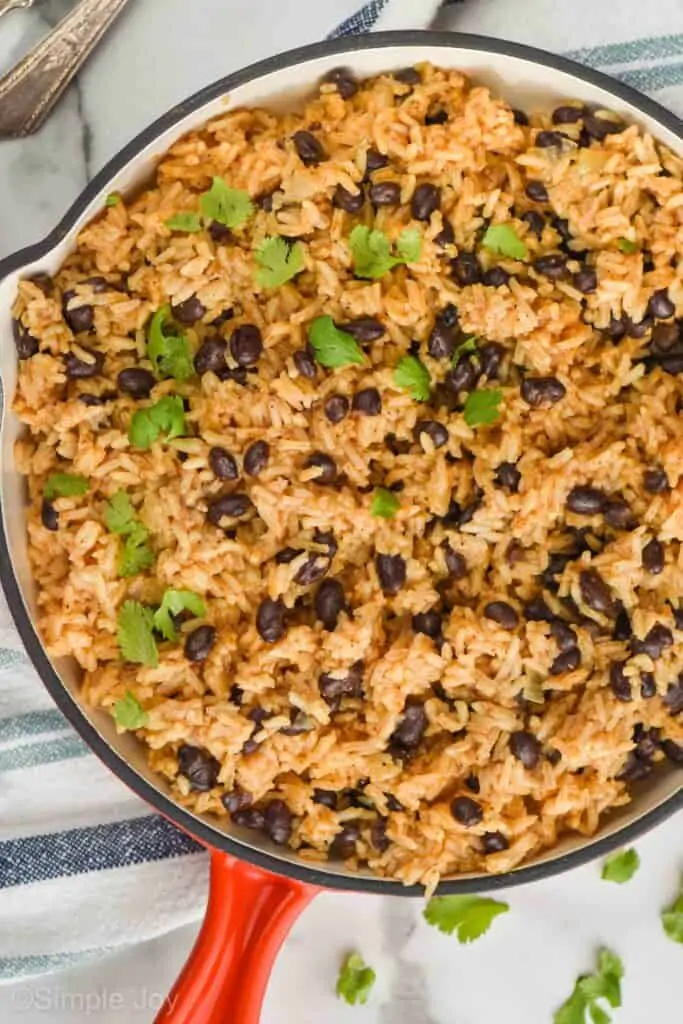 close up overhead view of a skillet with black beans and rice garnished with cilantro, a striped cloth napkin underneath