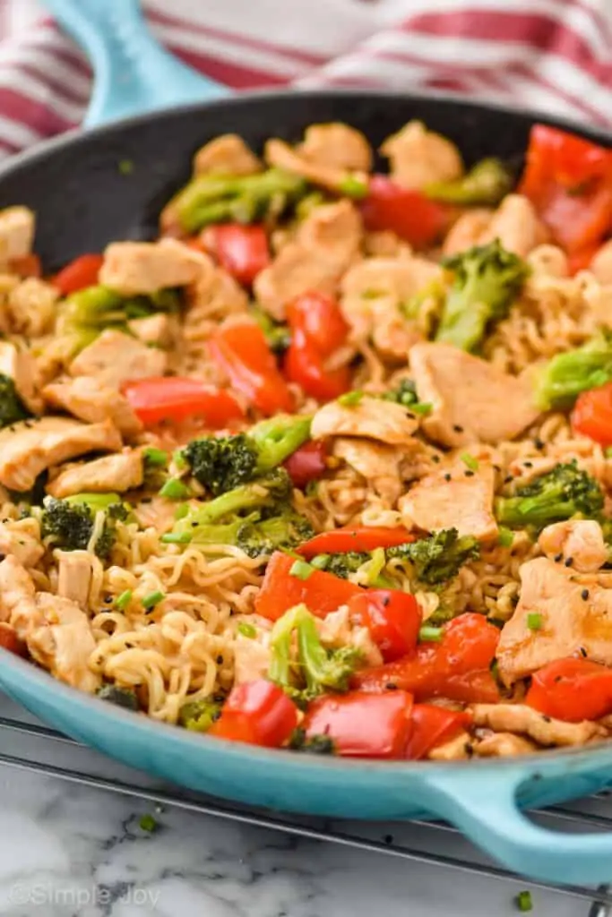 close up side view of a teal skillet holding ramen noodles, chicken, broccoli, and red pepper for stir fry dinner