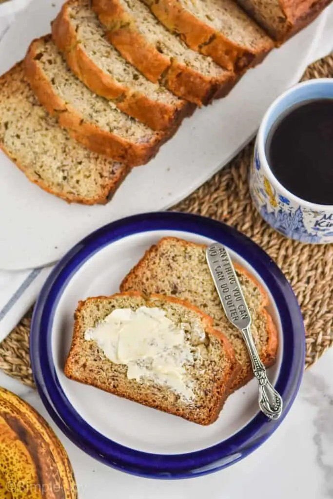 overhead view of two slices of banana bread on a blue rimmed plate, top piece has been buttered