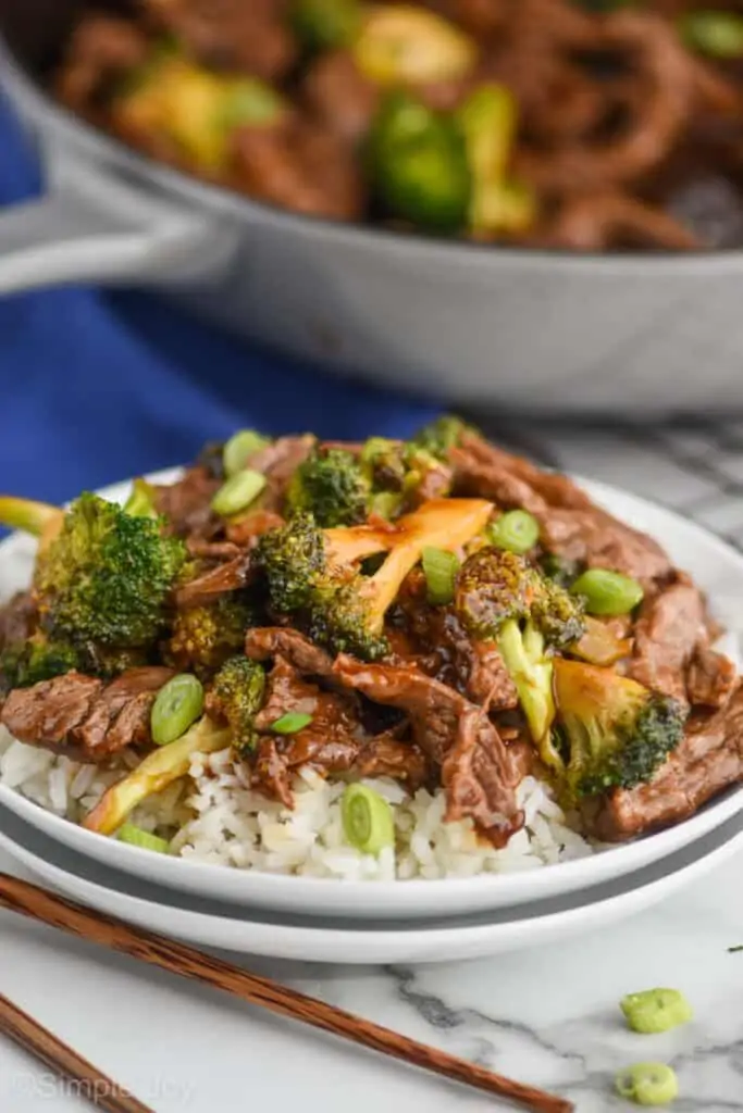 two small white plates stack with white rice and easy beef and broccoli on top of it, the rest of the skillet in the background