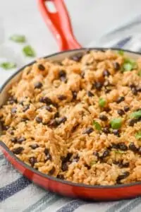 side view of a red skillet full of easy rice and beans recipe, garnished with cilantro