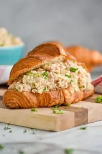 head on close up view of a ham salad sandwich recipe on a croissant on a cutting board with fresh parsley on it and around it