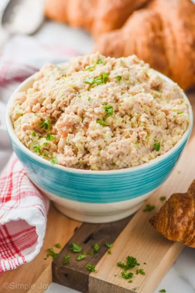 small white bowl with a turquoise stripe on a cutting board next to a red checked napkin filled with the best ham salad recipe