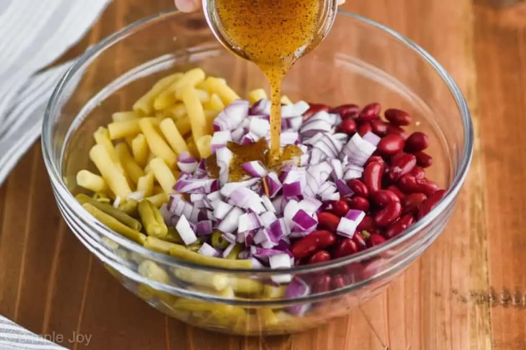 side photo of pouring salad dressing over three bean salad in a glass bowl