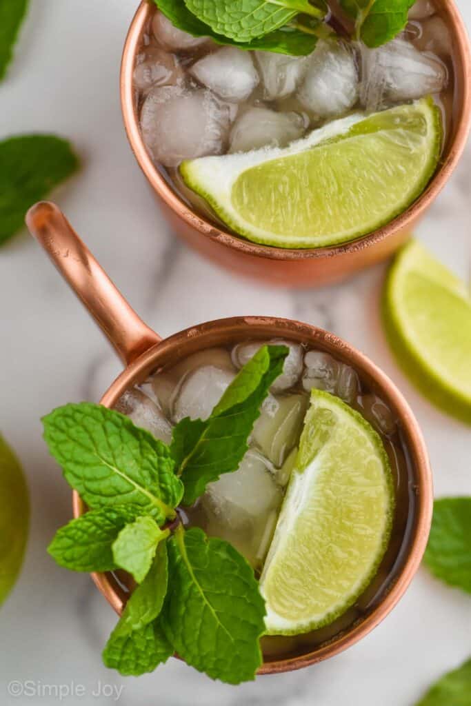 overhead view of two copper mugs filled with ice, garnished with lime wedges and fresh mint to make an Irish mule recipe