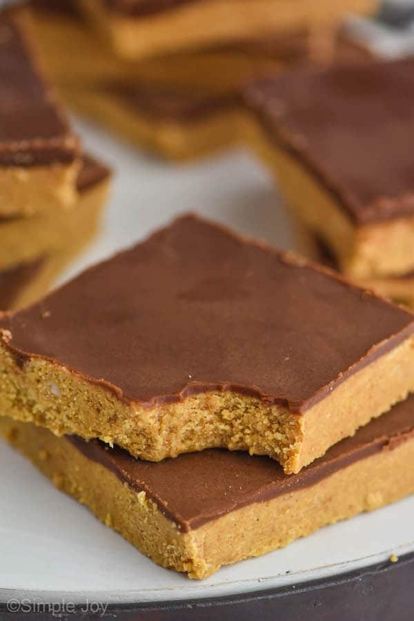two square chocolate peanut butters, one with a bite out of it stacked on another on a white surface, more in the background