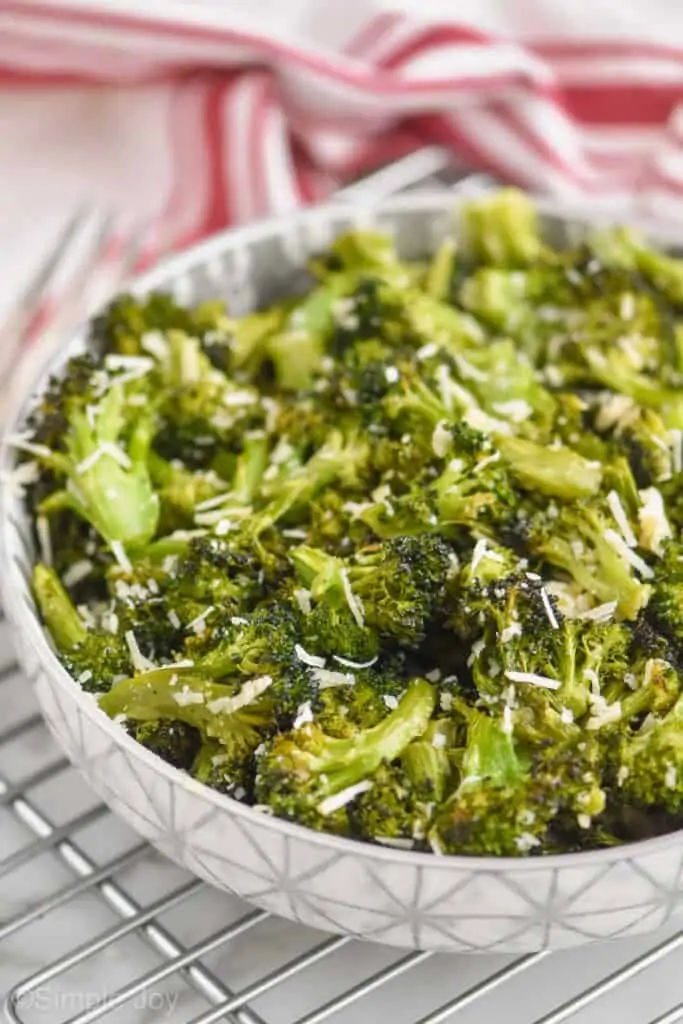 side view of a white bowl with a gray pattern on it filled with parmesan roasted broccoli and a red striped napkin the background