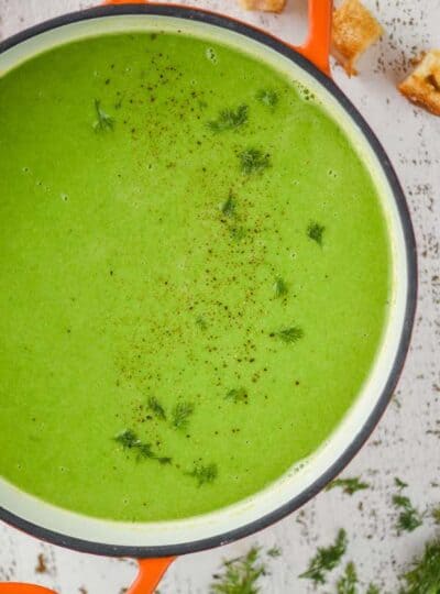 overhead view of a dutch oven with orange handles filled with pea soup garnished with fresh dill