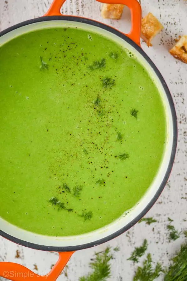 overhead view of a dutch oven with orange handles filled with pea soup garnished with fresh dill