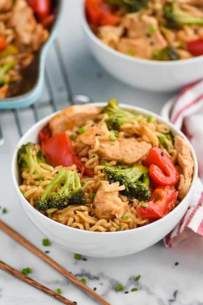 ramen stir fry in a small white bowl with broccoli, red peppers, noodles, and chicken