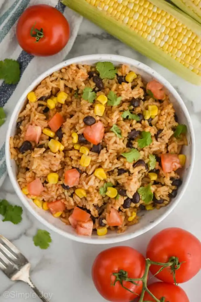 overhead view of a bowl of rice and beans garnished with diced tomatoes, corn, and cilantro