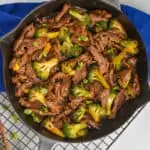 overhead photo of a gray skillet on a wire cool rack with a blue napkin holding beef and broccoli garnished with scallions