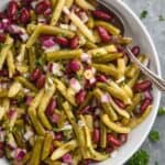 overhead of white bowl with three bean salad and a spoon in it on a gray surface garnished with parsley and on a cloth napkin - 9