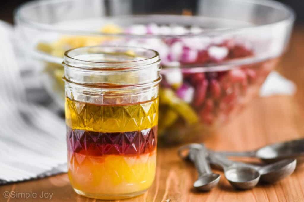 close up of a mason jar holding three bean salad dressing with the bowl of the salad in the background