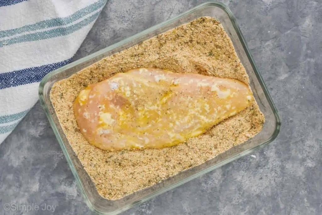 a chicken breast that has been covered in egg in a rectangular baking dish in breadcrumbs