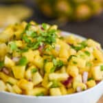 up close view of a white bowl full of pineapple salsa topped with chopped cilantro, with diced jalapeño and red onions