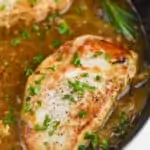 a pan fried pork chop in a a frying pan, with easy onion sauce around it and chopped parsley on top