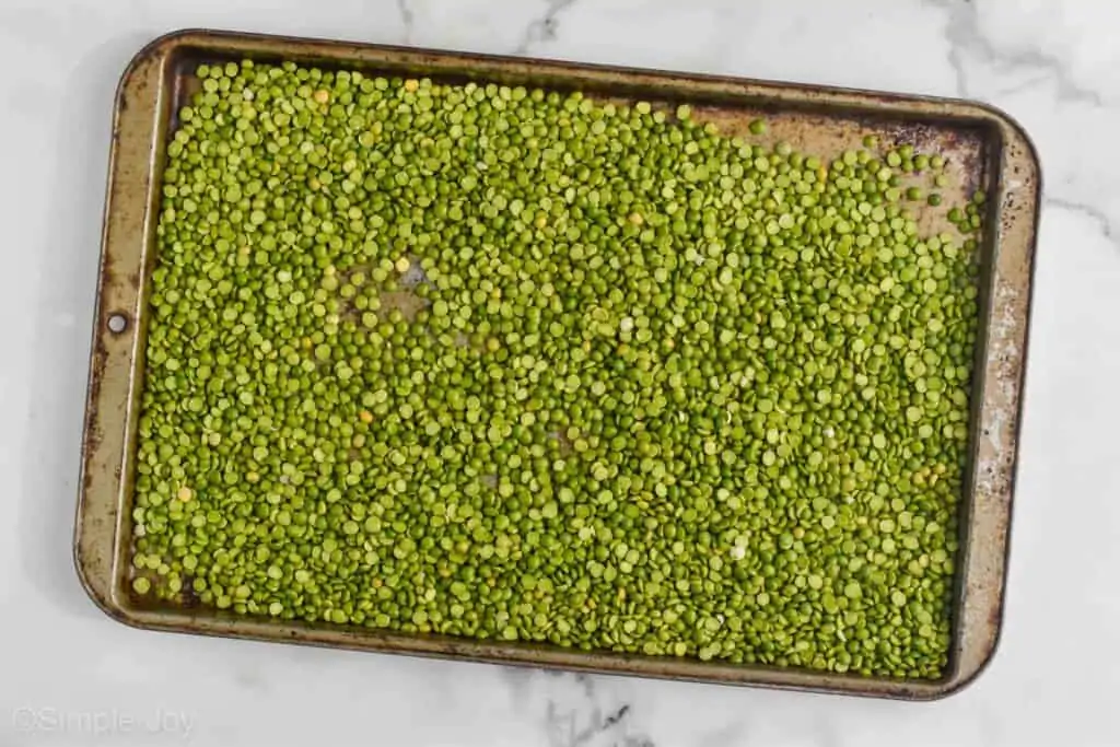a galvanized baking sheet filled with dry split green peas on a white marble countertop
