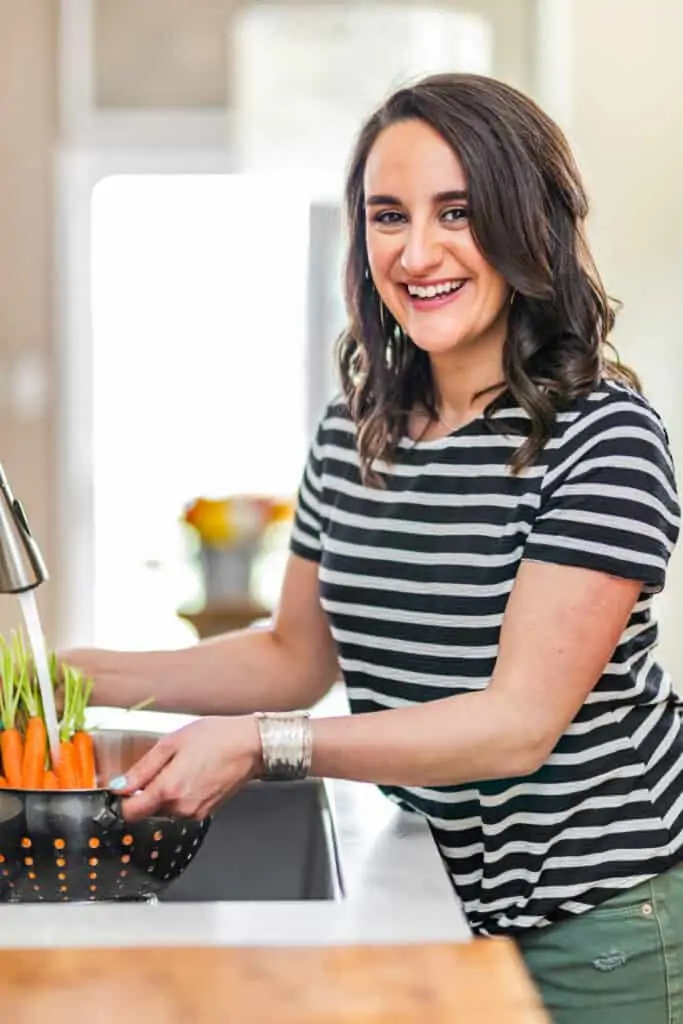 woman in a striped shirt washing carrots in a sink