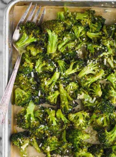 overhead view of a rimmed baking sheet with parchment paper and roasted broccoli that has parmesan on it