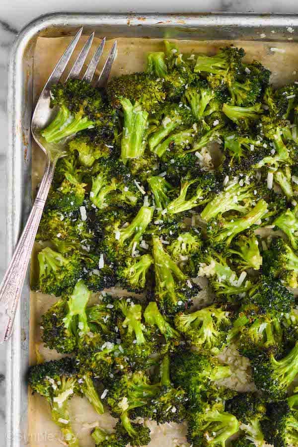 overhead view of a rimmed baking sheet with parchment paper and roasted broccoli that has parmesan on it
