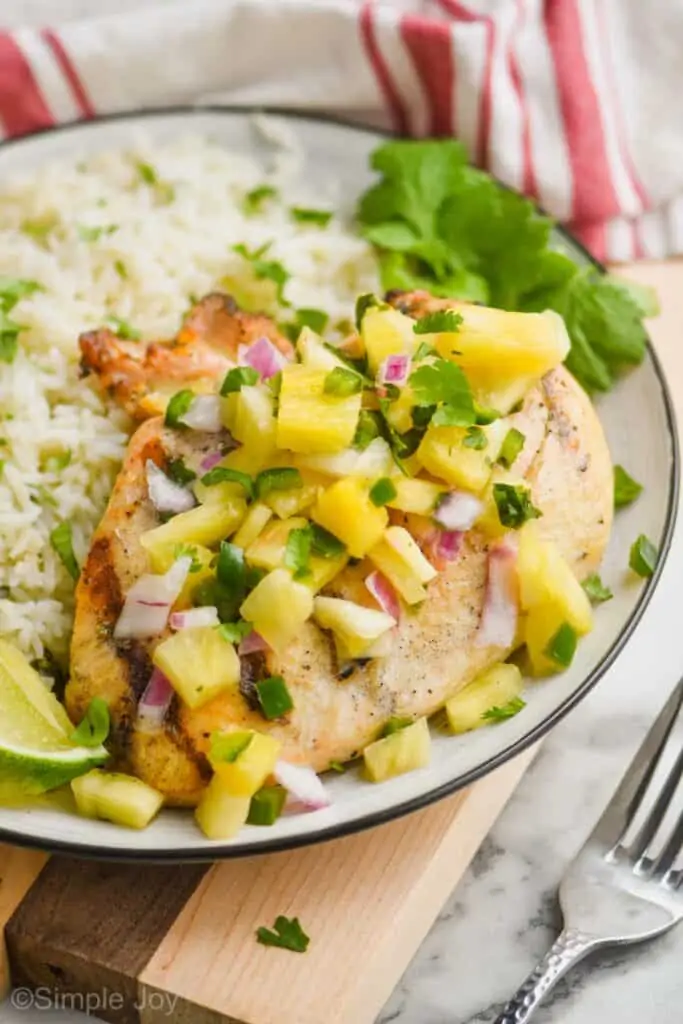 close up side view of the best marinated grilled chicken breast that is covered in pineapple salsa with fresh cilantro next to it on a plate