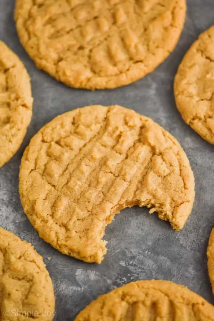 close up of a an easy peanut butter cookie on a gray surface surrounded by other peanut butter cookies, the one in the middle has a bite missing