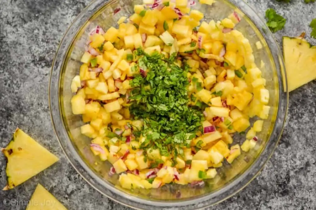overhead view of pineapple salsa being mixed with a lot of fresh cilantro on top
