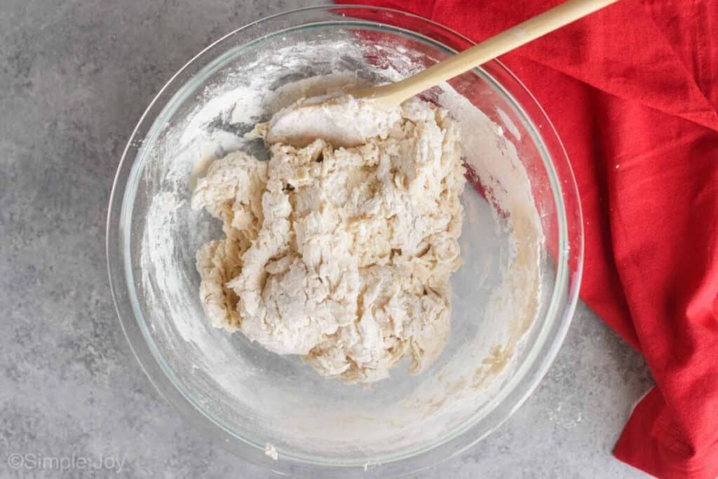 overhead view of sandwich bread dough coming together, rough and shaggy with a wooden spoon