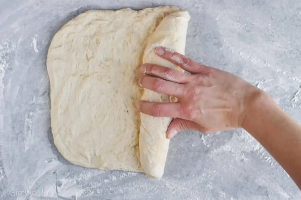 a hand rolling up dough for sandwich bread recipe