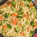 a close up of a teal skillet that has vegetables and spaghetti in it and is garnished with green onion slices and sesame seeds