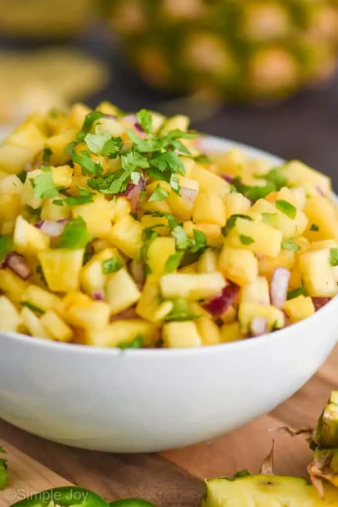 up close view of a white bowl full of pineapple salsa topped with chopped cilantro, with diced jalapeño and red onions