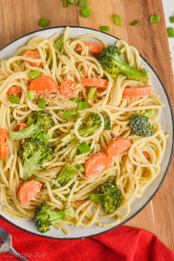 a close up of a plate of spaghetti that has vegetables in it and a hummus based sauce