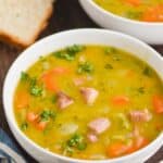 a white bowl on a wood surface full of split pea soup, garnished with fresh parsley - 6