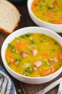 a white bowl on a wood surface full of split pea soup, garnished with fresh parsley