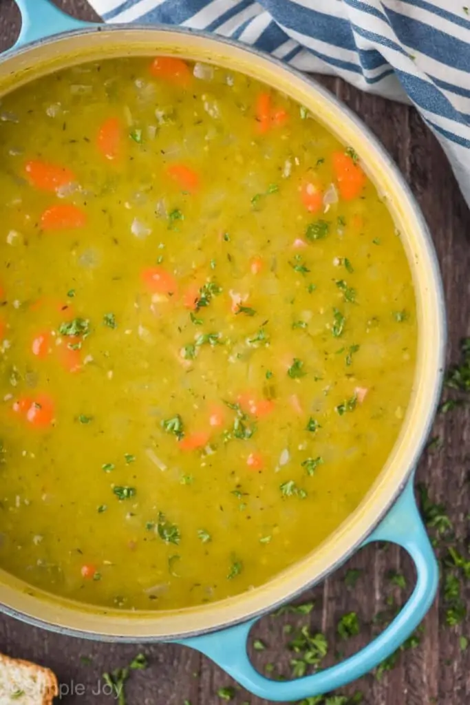overhead view of a teal dutch oven full of split pea and ham soup with lots of fresh parsley on top