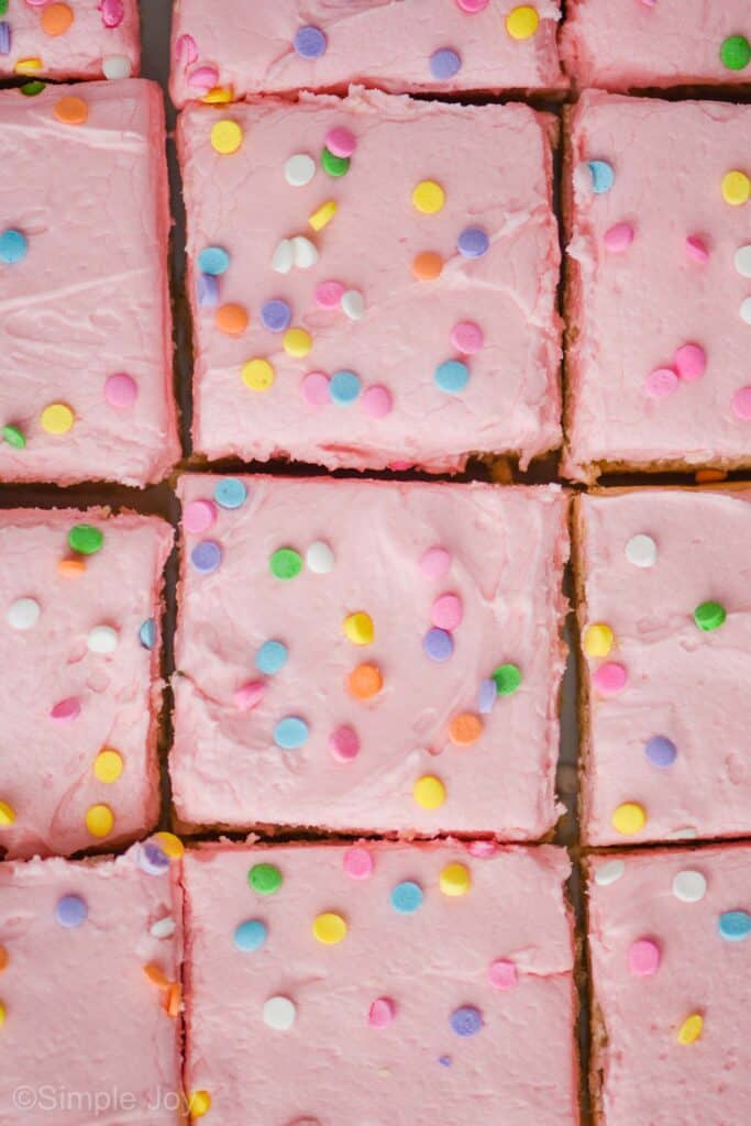 overhead view of sugar cookie bars that are cut and close together, frosting with pink frosting and pastel circle sprinkles